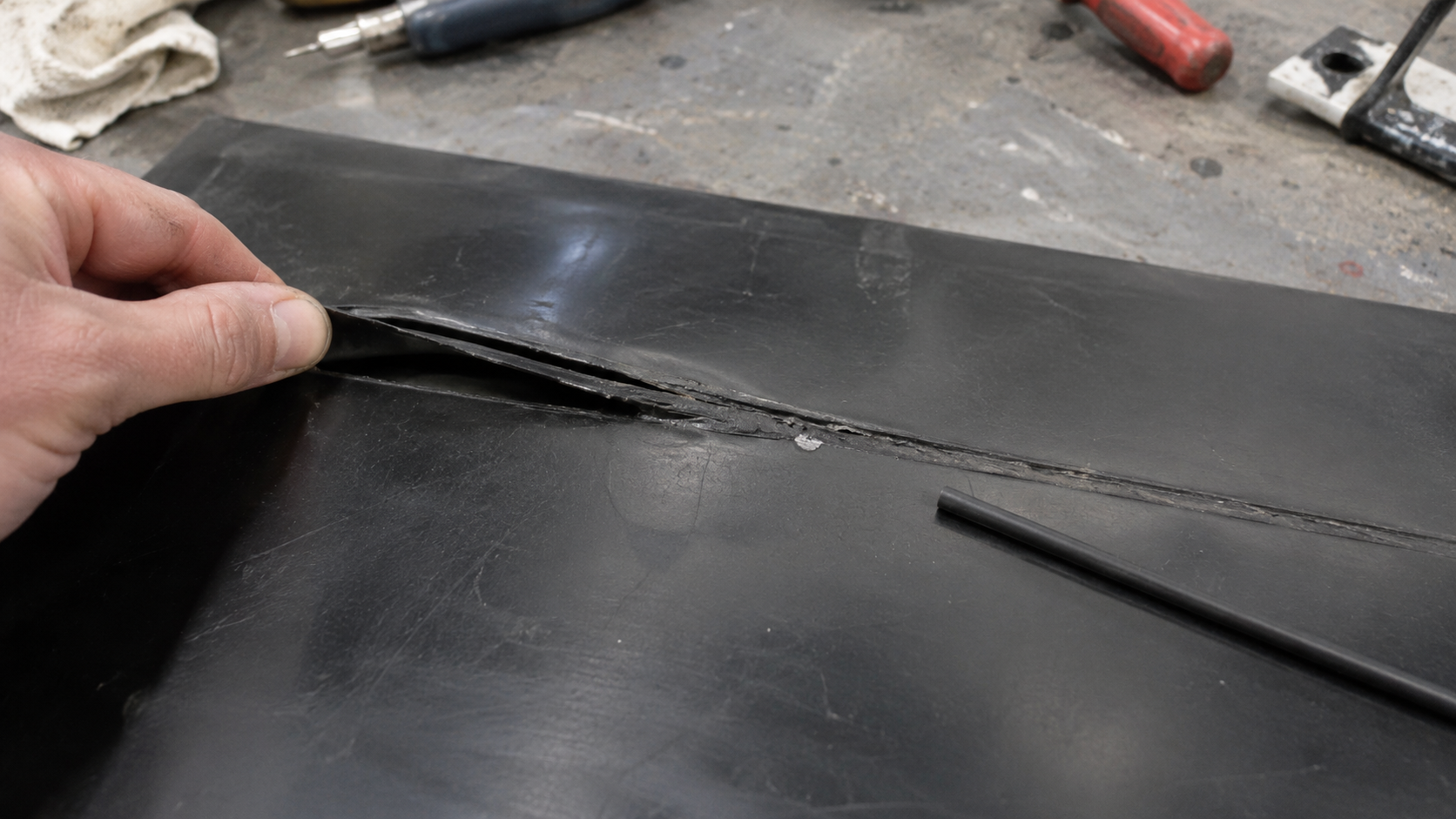 Failed PE welding rod bond separating from black HDPE sheet during weld inspection