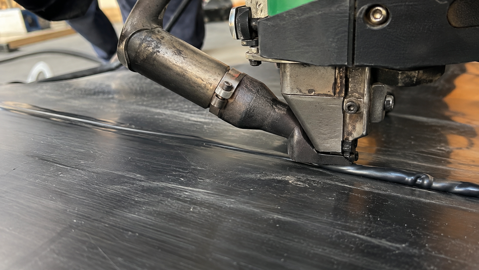 Close-up of HDPE extrusion welding with molten PE weld bead on black plastic sheet
